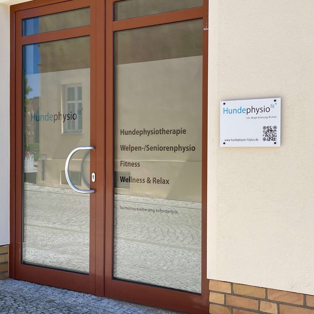 Eingang Hundephysio Fitplus Eingang zur Hundephysio Fitplus-Praxis mit Fenstern und einem Schild für die Physiotherapie.